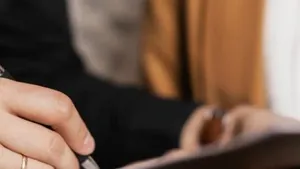 A hand signing a document on a desk beside a notebook