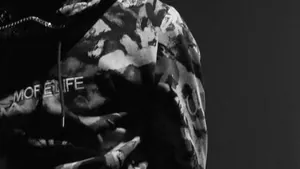 A rapper in a camouflage hoodie holding a microphone while freestyling, in black and white