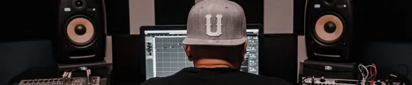 A producer in dark clothes and headphones lit from one side in a dark room