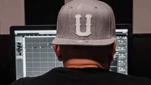 A producer in dark clothes and headphones lit from one side in a dark room