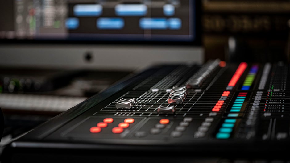 Close-up of a mixing console with a DAW open behind it