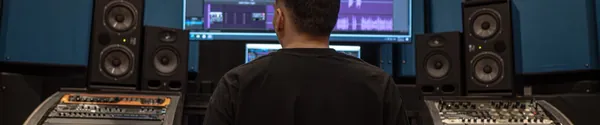 Producer sitting in a dark control room facing a screen full of tracks