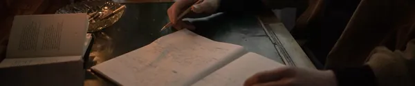 Person writing rap lyrics in a notebook next to a laptop