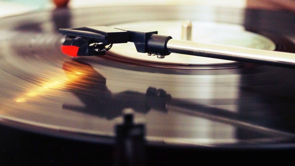 Close-up of a record player stylus riding a spinning vinyl record in warm light