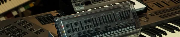 A synthesizer sitting on top of a piano keyboard in a dim studio