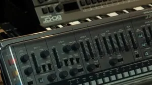 A synthesizer sitting on top of a piano keyboard in a dim studio