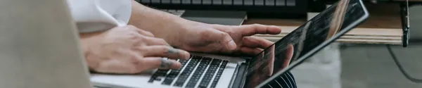 A producer working on a laptop in front of a keyboard and synth in a home studio
