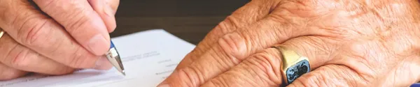 Hands signing a document on a wooden desk