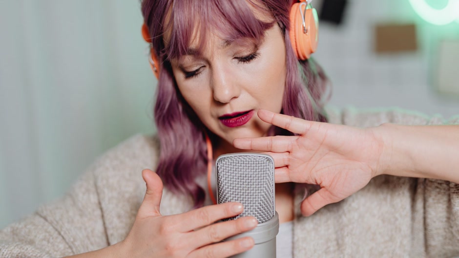 A singer with headphones recording vocals in a dark studio