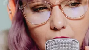 A singer leaning into a microphone lit by purple neon light in a studio