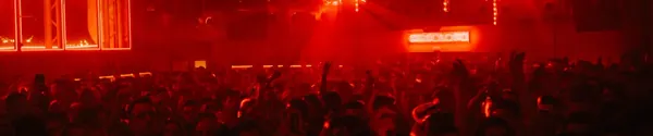 A crowd in a nightclub lit by red stage lights during a concert