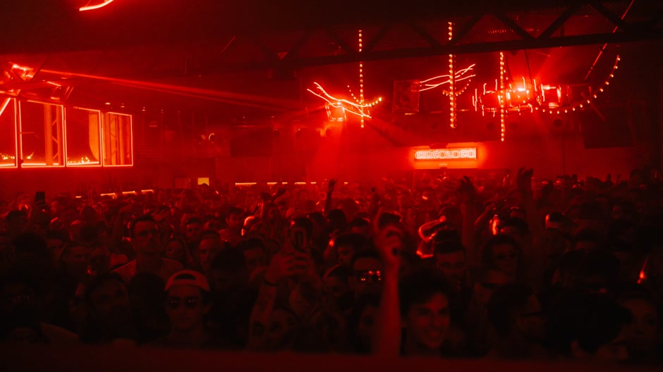 A crowd in a dark club lit by red lights during a live show